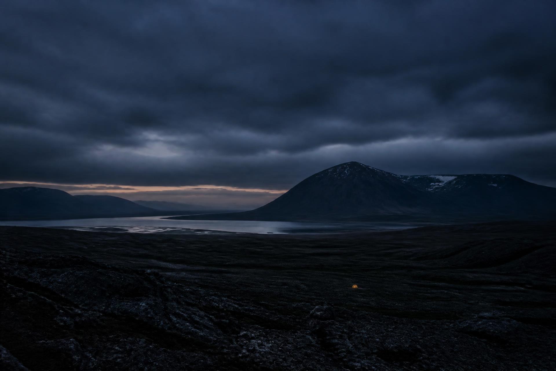 A single illuminated tent dwarfed by mountains and sky at dusk in Sweden